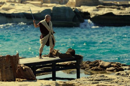The Praetorian, played by Barry Aird, stands on a jetty at the beach at Herculaneum with his sword raised. (National Geographic/Darrin Zammit Lupi)