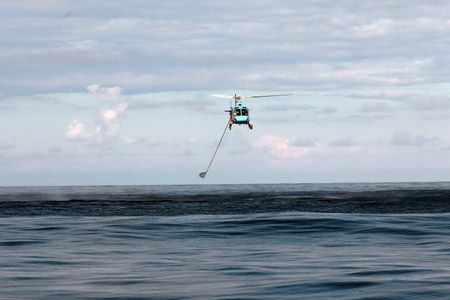 The helicopter flies over the water with Aldo Kane holding out a net. (National Geographic/Mario Tadinac)