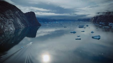 A boat cruising through calm waters and surrounding icebergs, heading towards the climb.(photo credit: National Geographic/Simon Niblet)