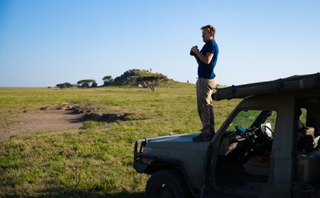 Bertie Gregory stands on the front bonnet of a safari Jeep looking for animals. (credit: National Geographic/Jigar Ganatra)