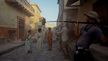 Behind-the-scenes showing Buket Komur (Amalthea), Lubna Azabal (Julia Felix), and Frankie Treadaway (Avianius) filming a recreation scene with Director of Photography Jim Jolliffe operating the main camera and support crew behind him. (National Geographic/Matthew Muscat Drago)