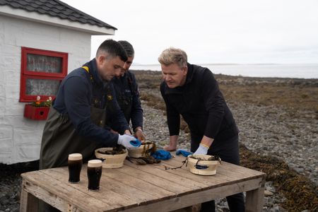 Michael Kelly Jr. and Michael Kelly Sr. shuck oysters as Gordon Ramsay looks on. (National Geographic/Justin Mandel)