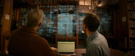 Professor Steven Tuck and Tom Hiddleston sit at a desk in a classical library, viewing a database of Roman artifacts and inscriptions. (National Geographic)