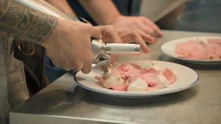 Chef Diego Rossi (L) sprays tuna mousse on veal slices, preparing his renowned dish 'vitello tonnato'.   (credit: National Geographic)