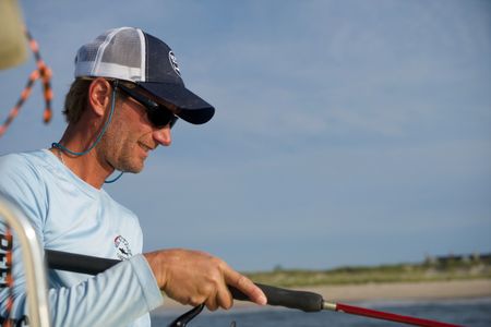 Capt. Greg Metzger glances to the water as he reels in menhaden, the baitfish used to catch baby white sharks. (National Geographic/Brandon Sargeant)