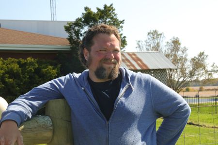 Charles Pol leans on a wooden fence in the sun at the Pol family's farm. (National Geographic)