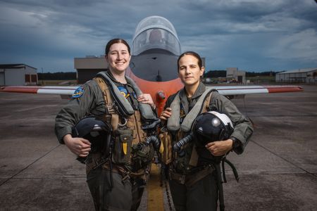 Students LT Carissa Meinster and Captain Steph Harris pose behind a T-45. (Credit: National Geographic/Freddie Claire)
