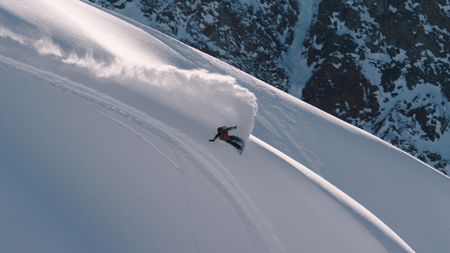 Travis Rice raises powder snow with his snowboard as he goes down a mountain in Alaska.  (photo credit: Travis Rice, Inc)
