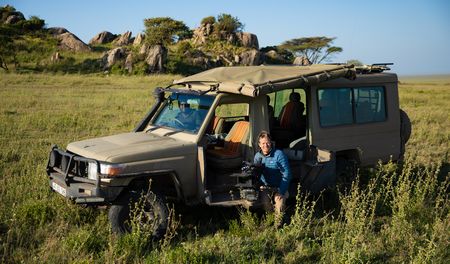 Bertie Gregory sits in front of a safari Jeep holding a camera. (credit: National Geographic/Jigar Ganatra)