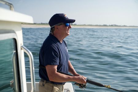 Dr. Greg Skomal, stands reeling in his rod, on a sunny day fishing for menhaden just of the shore of Long Island. (National Geographic/Brandon Sargeant)