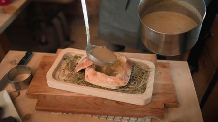Franz Mulser serves his signature hay soup in a loaf of homemade bread, inside the hut of his restaurant Gostner Schwaige.  (credit: National Geographic)