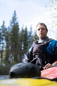 Kneeling by the river, professional kayaker Ben Stookesberry looks straight at the camera with the lake as his background.  (National Geographic/Harrison Gayton)