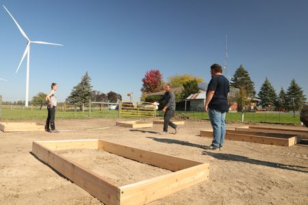 Beth Pol, Ben Reinhold, and Charles Pol use a tape measure to measure and spray paint to mark the distance between the wooden frames in the Pol family farm's new garden. (National Geographic)