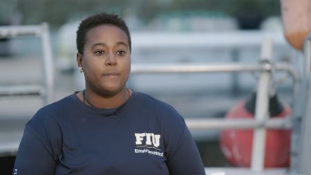 Candace Fields, expert, speaking to camera about Love Key in Florida and how due to the waters in this location being a protected marine area the waters tend to have a healthy amount of fish population and how this attracts various types of sharks. (National Geographic)