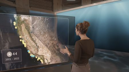 Dr. Diva Amon next to a GFX map of California and a chart of shark attacks whilst in the shark lab studio. (National Geographic)