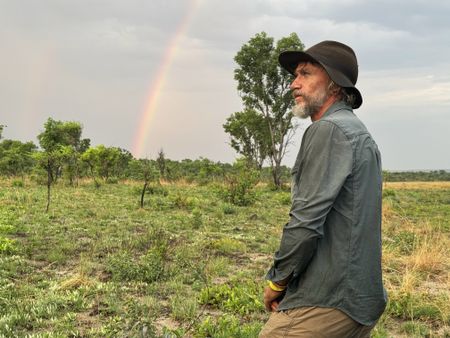 Dr. Steve Boyes, with a rainbow in the background, experiences the first signs of the rainy season. (Credit: Ariel Leon Isacovitch)