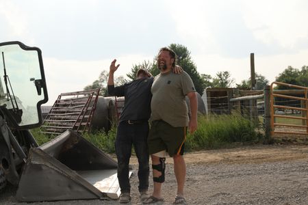 Ben Reinhold and Charles Pol, in a leg brace, laugh together as they work on a swale to prevent flooding around the sheep hut. (National Geographic)