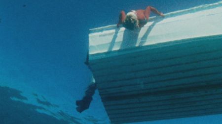 Valerie Taylor leaning over the boat looking into water in 1968. Shot from underwater. (photo credit: Ron & Valerie Taylor)