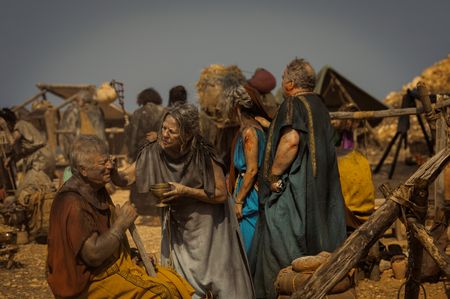 An elderly woman cleans an elderly man's head wound at the Pompeii displacement camp, while Cassius and his wife pass by in the background. (National Geographic/Darrin Zammit Lupi)
