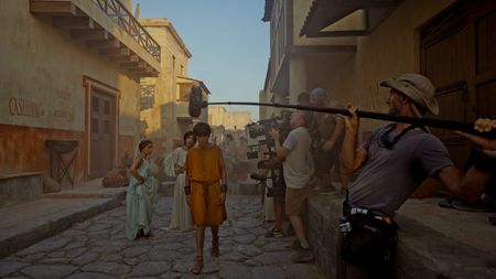 Behind-the-scenes showing Buket Komur (Amalthea), Lubna Azabal (Julia Felix), and Frankie Treadaway (Avianius) filming a recreation scene with Director of Photography Jim Jolliffe operating the main camera and support crew behind him. (National Geographic/Matthew Muscat Drago)