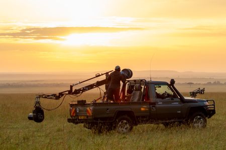 Faith Musembi stands in the back of the film vehicle, working with the crew as they wait for lions to enter into frame. (National Geographic/Abigail Brown)