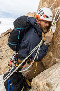 Aldo Kane hugs the rock during an ice fall on Pool Wall in Eastern Greenland.  (photo credit: National Geographic/Matt Pycroft)
