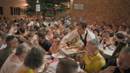 A waiter serves hot food from a tray to a participant at a bustling Palio dinner, held on the lively streets of Siena on the eve of the famed race.  (credit: National Geographic)
